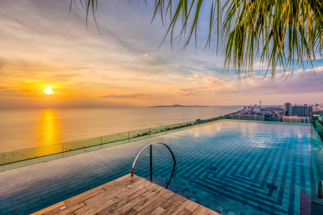 Rooftop infinity pool at sunset overlooking Pattaya bay with palm fronds framing the horizon