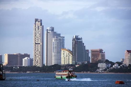 Pattaya beachfront skyline at dusk with high-rise condominium towers and a tourist boat crossing the bay